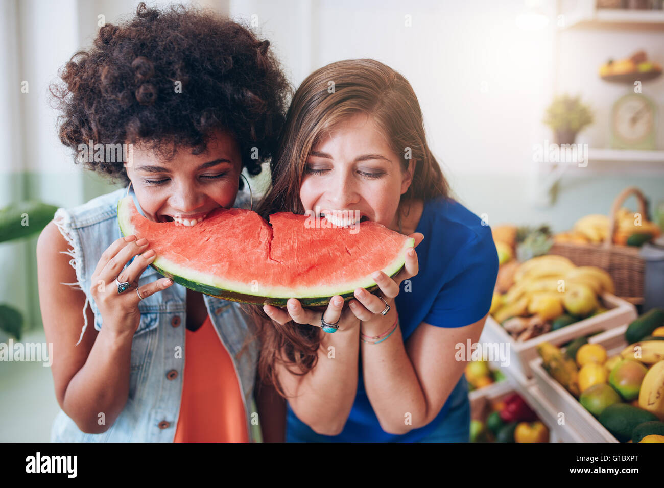 Two young woman eating watermelon and having fun. Mixed race female friends together eating a watermelon slice. Stock Photo