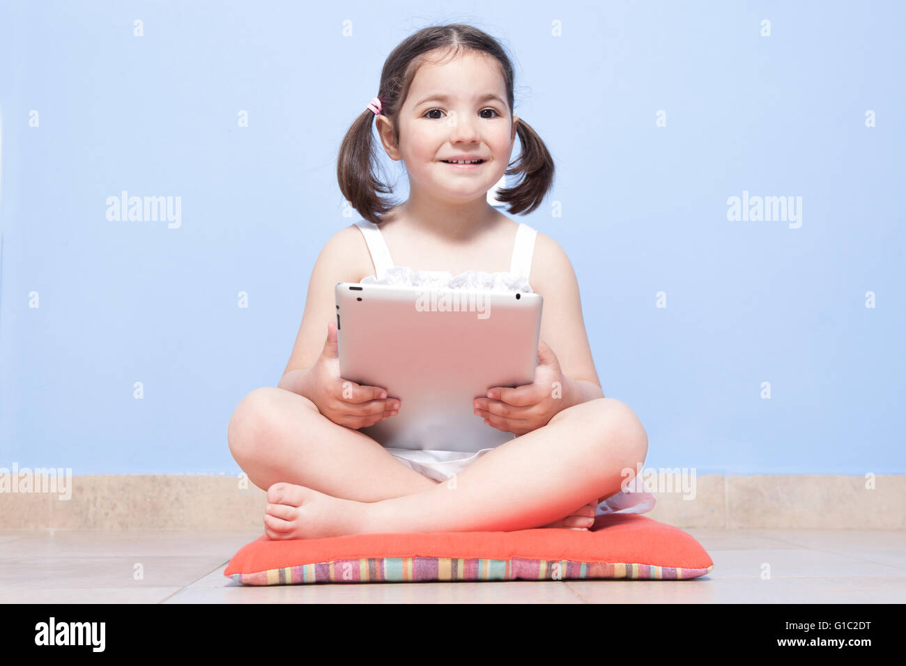 Smiling little girl sitting in her room floor using tablet computer Stock Photo