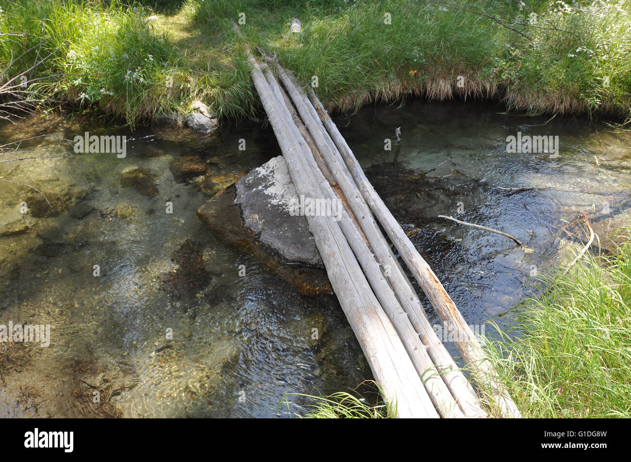 a small simple bridge spanning a mountain stream made of four wood poles Stock Photo