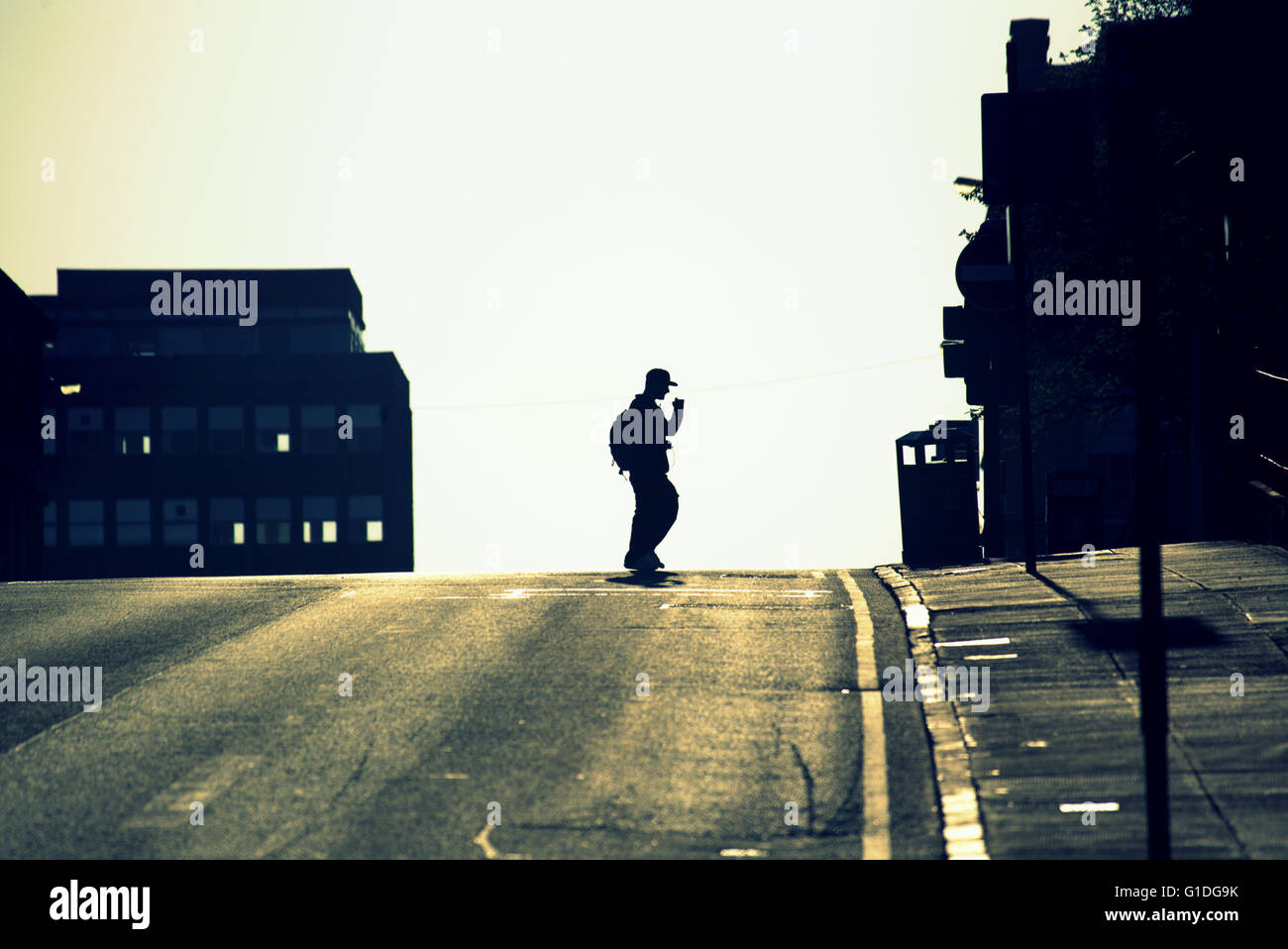 Silhouette of man on mobile phone with backpack on Glasgow street with road contre- jour backlit in  Glasgow,Scotland, UK. Stock Photo
