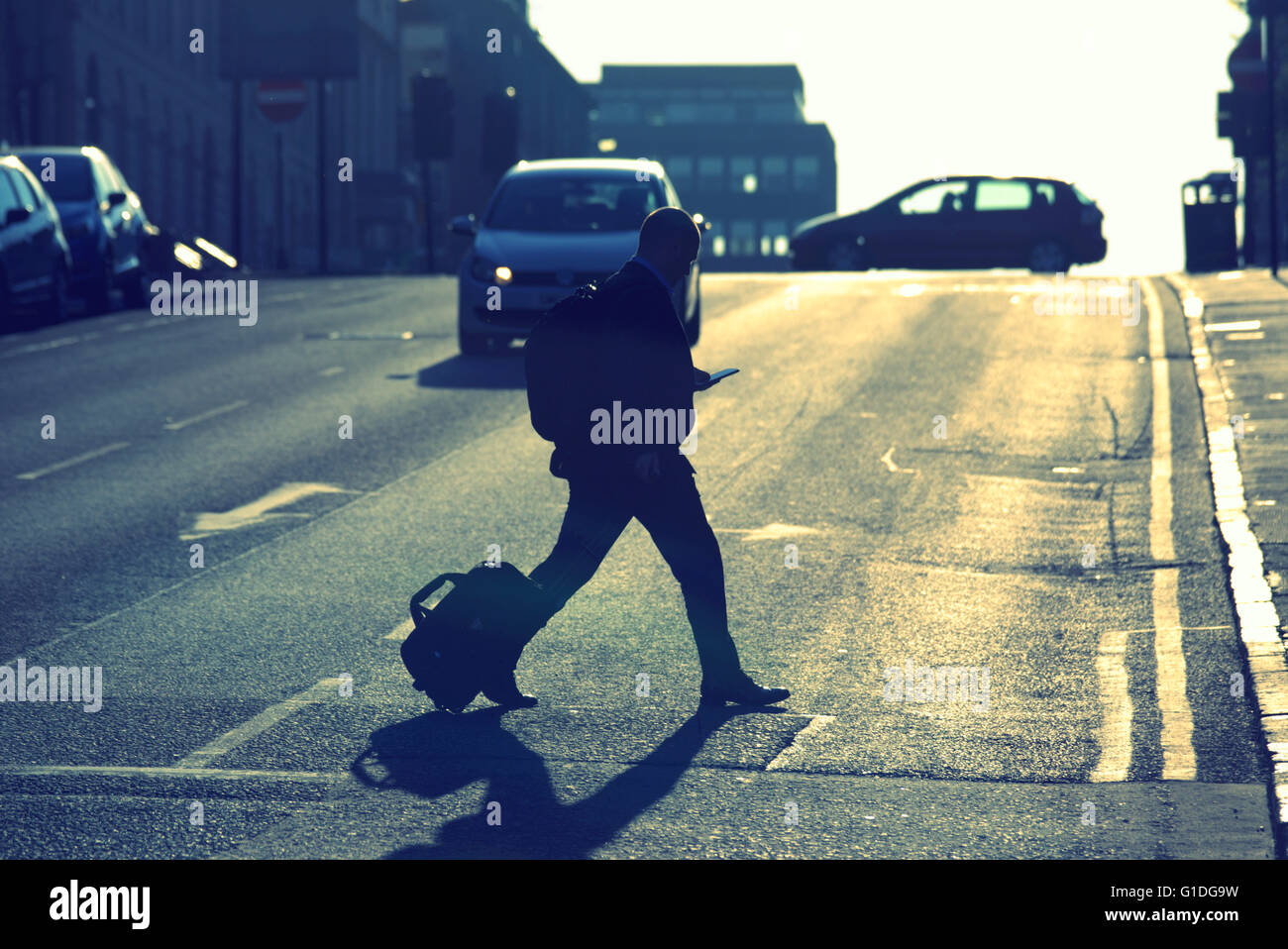 Silhouette of man on mobile phone with case on Glasgow street with road contre- jour backlit in  Glasgow,Scotland, UK. Stock Photo