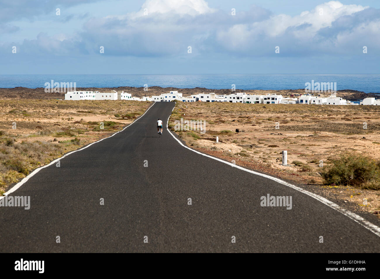 Cyclist on road approaching Caleta de Caballo village, Lanzarote, Canary islands, Spain Stock Photo
