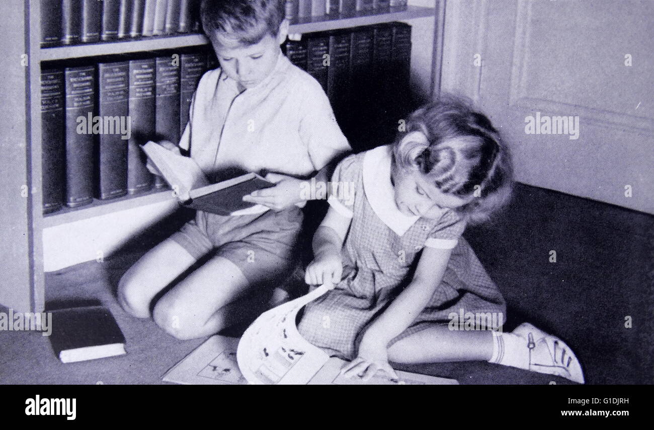 photograph showing a young boy and girl seated reading books. 1955 Stock Photo