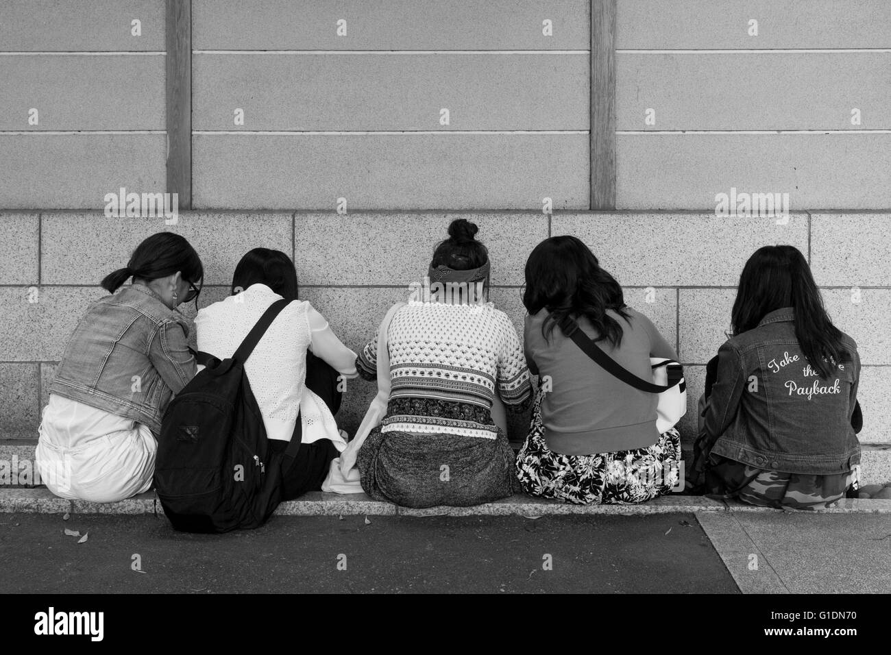 Five women sitting on the pavement facing a wall. Kamakura, Japan Stock Photo