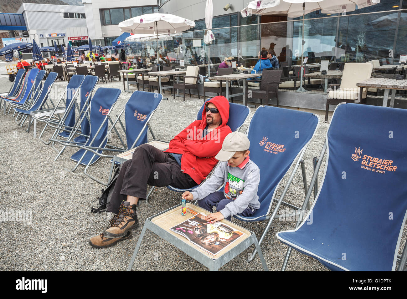 Father and son relaxing on a lounge chair on the top of Stubai Glacier Stock Photo