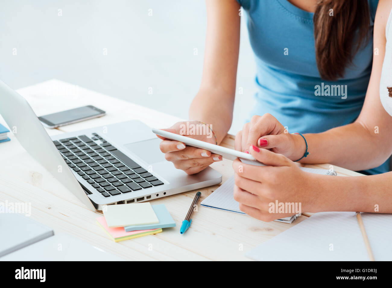 Teen girls sitting at desk and using a touch screen tablet, they are studying and using apps, hands close up Stock Photo