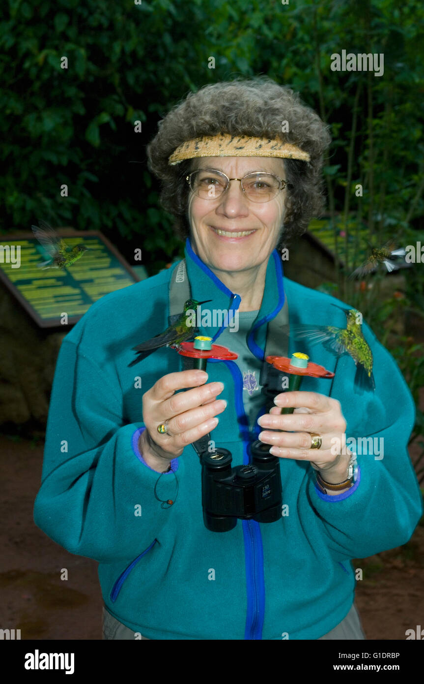 Woman holding hummingbird feeders attracting birds, La Paz Waterfall Gardens, Costa Rica Stock Photo
