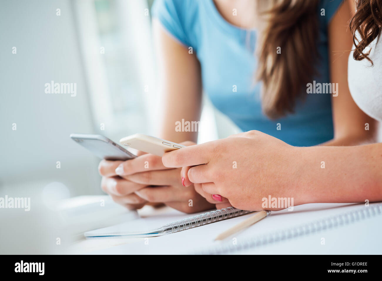 Teenager female students sitting at desk, studying and using touch screen smart phones, youth culture and telecommunications con Stock Photo