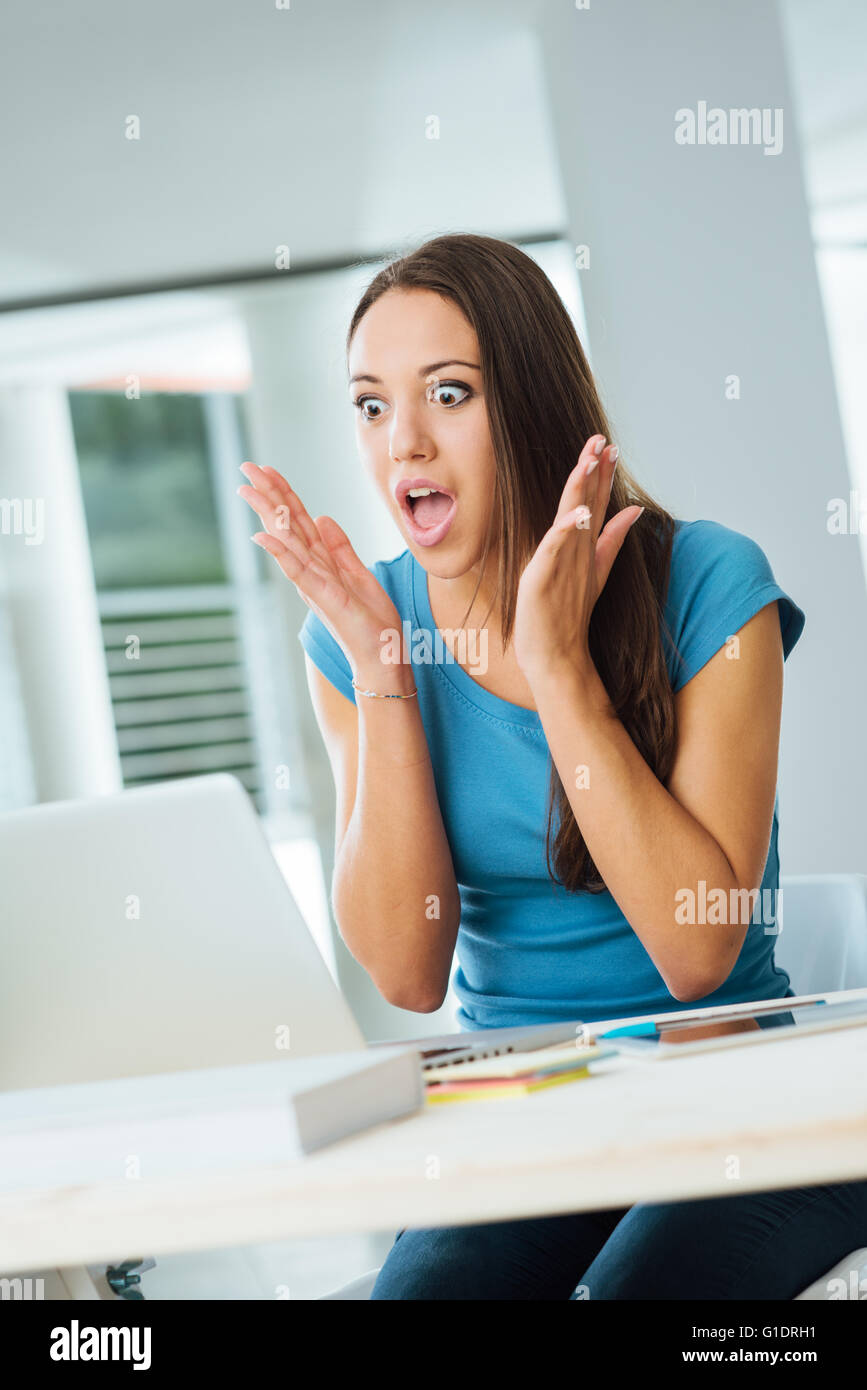 Shocked astonished young woman at desk having troubles with her computer Stock Photo