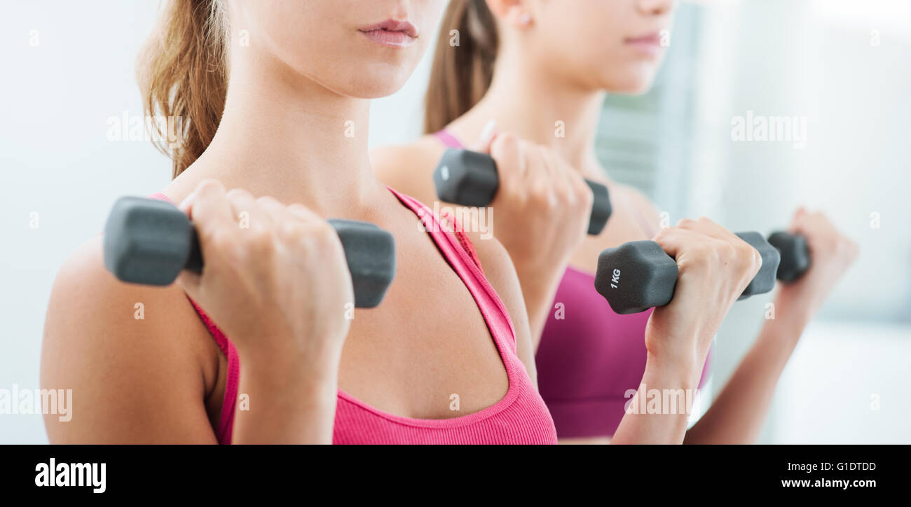Confident young women exercising and weightlifting at the gym using dumbbells, workout and fitness concept Stock Photo