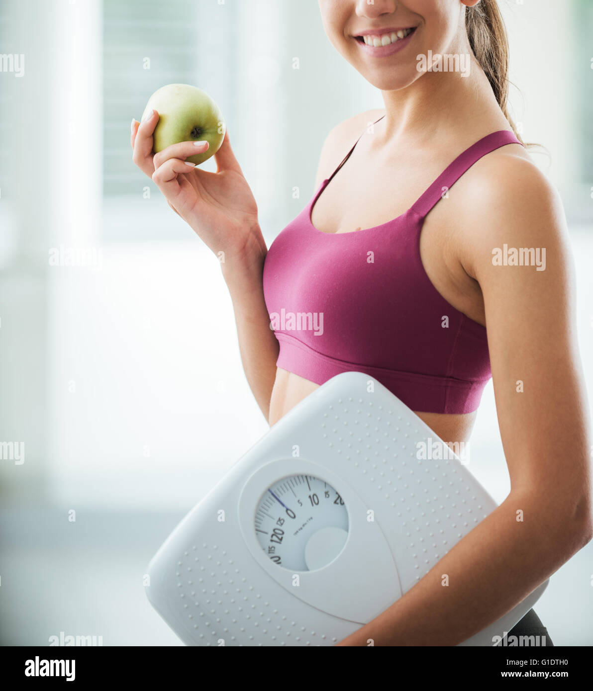 Smiling teenage girl holding a scale and a fresh apple, healthy eating, fitness and weight loss concept Stock Photo