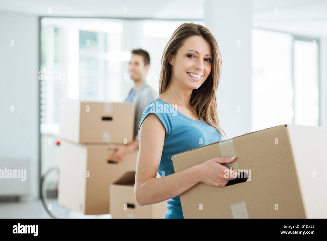 Happy smiling couple moving in a new house and carrying carton boxes ...