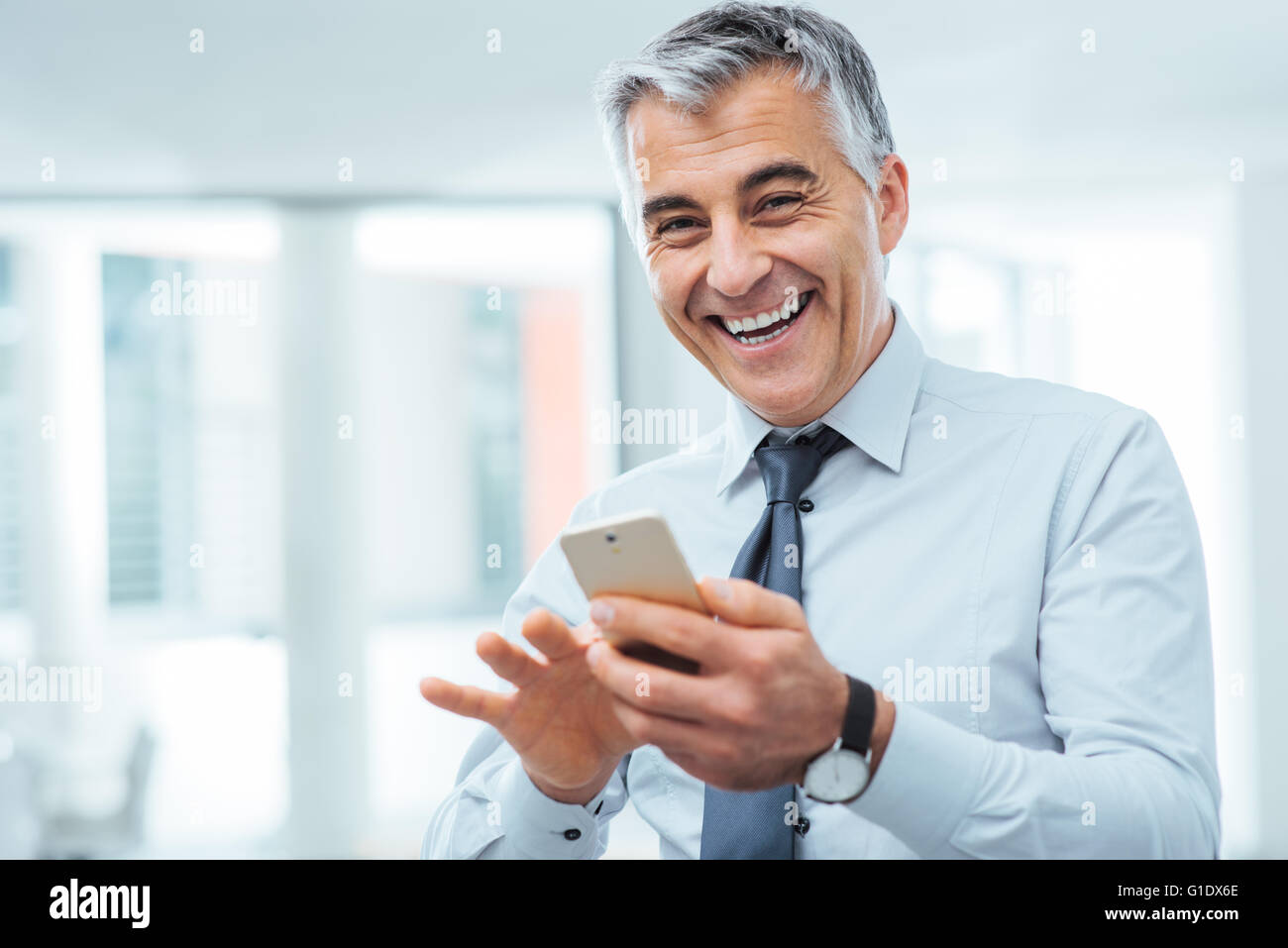 Smiling cheerful businessman using a touch screen smart phone and ...