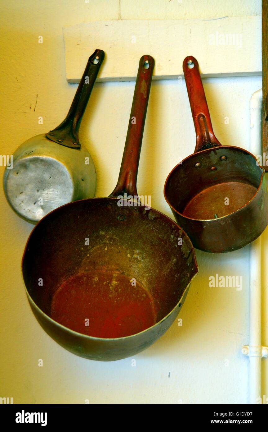 Three old casseroles in scrap hung has a wall on a piece of wood. Stock Photo