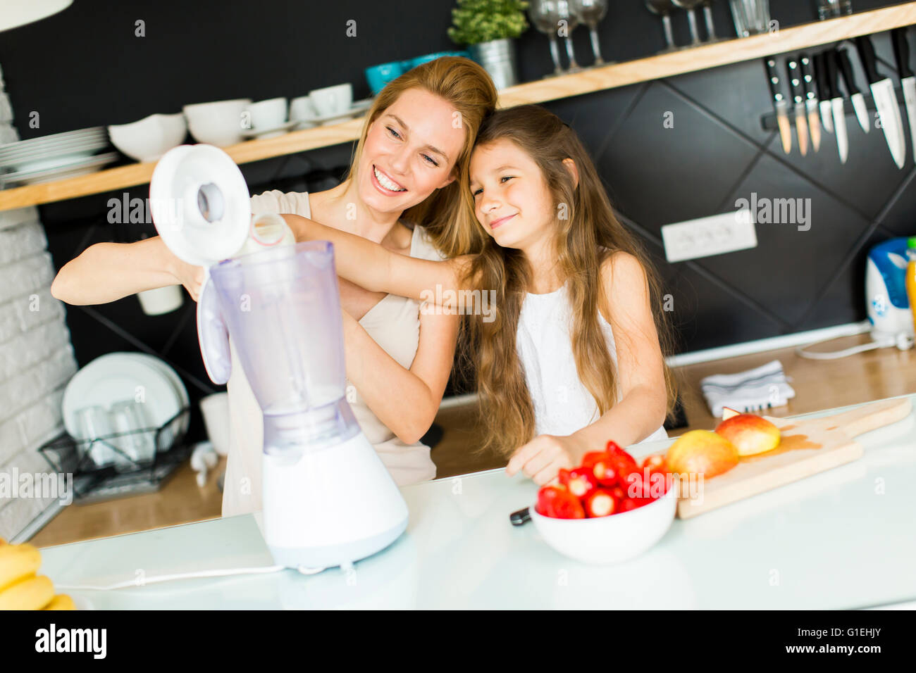 Mother and daughter blending smoothie from fresh fruits in the modern kitchen Stock Photo