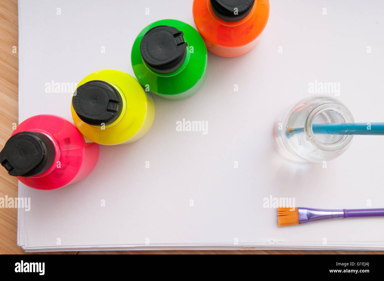 Paint brush in water in front of brightly coloured children's paint