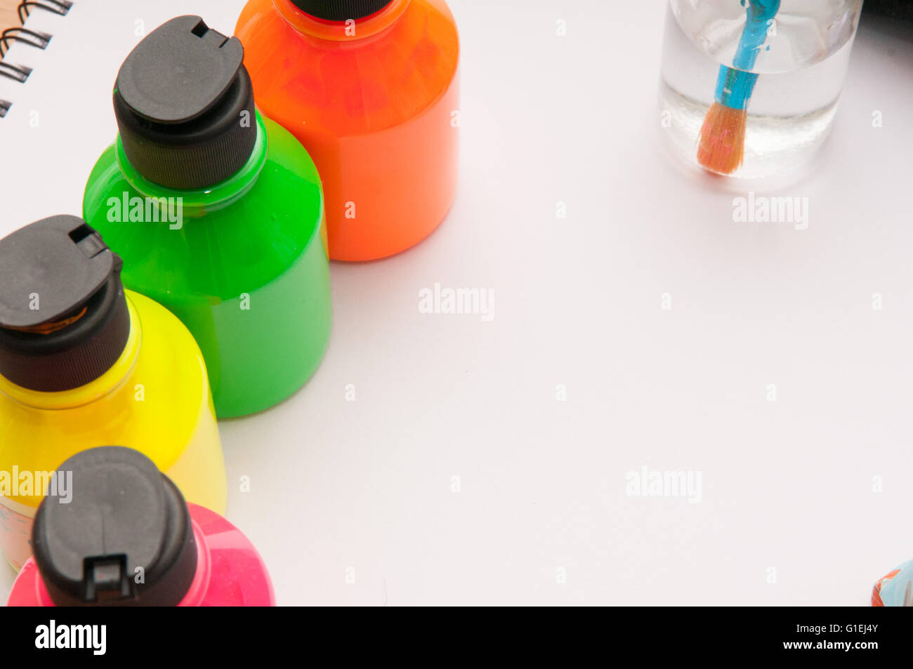 Paint brush in water in front of brightly coloured children's paint