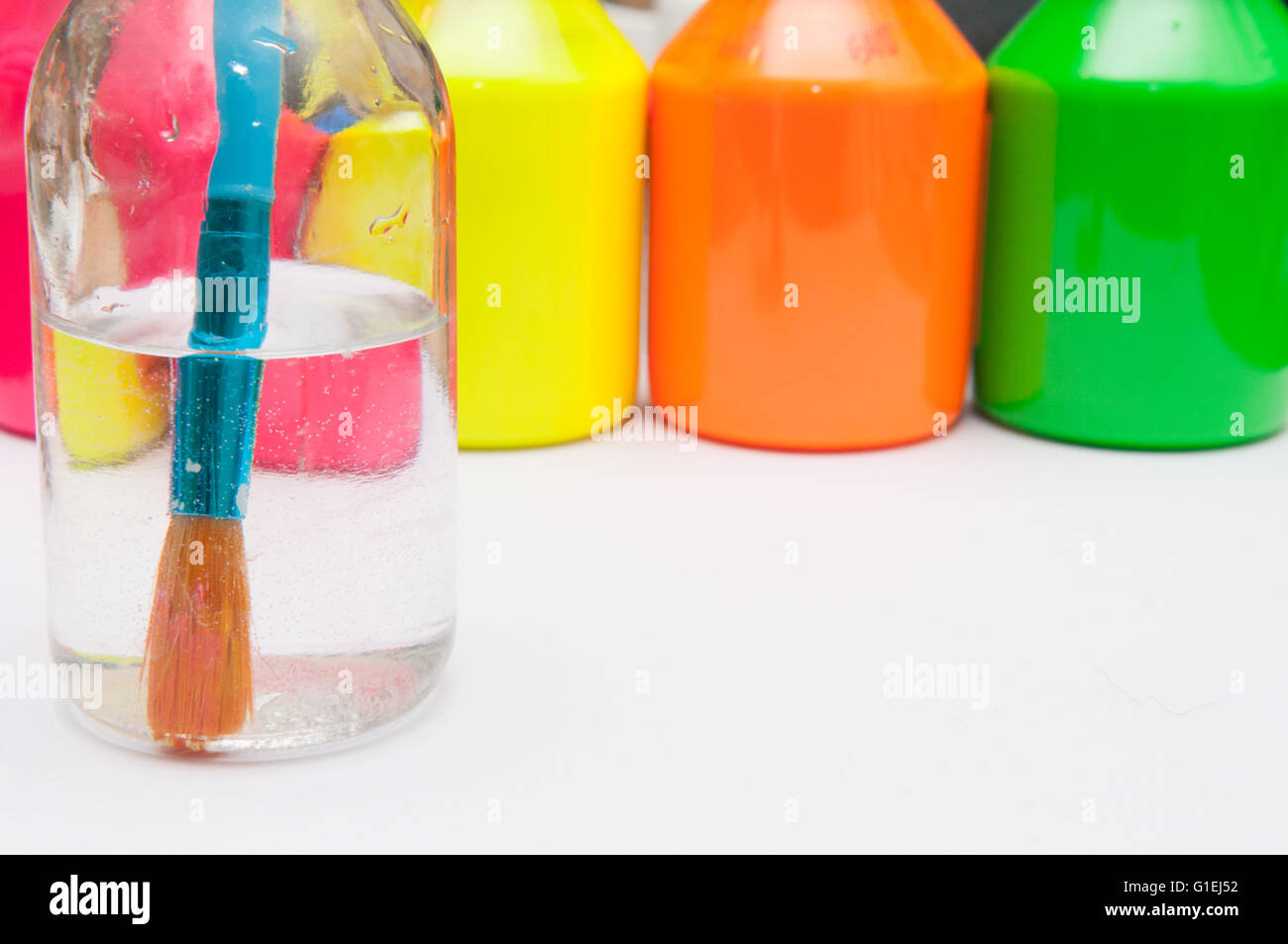 Paint brush in water in front of brightly coloured children's paint