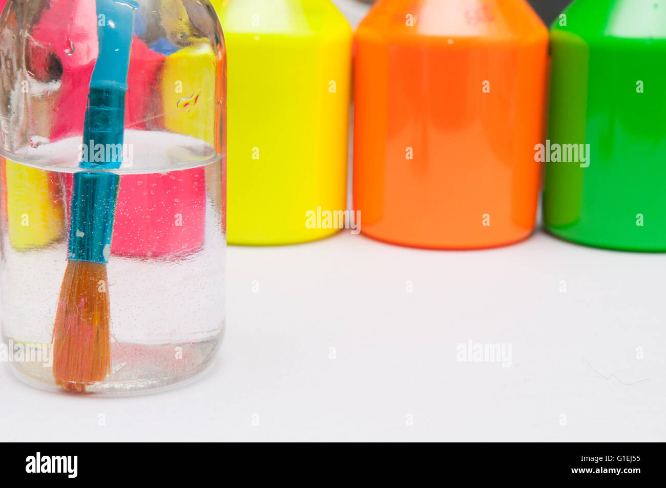 Paint brush in water in front of brightly coloured children's paint pots for a rainy day