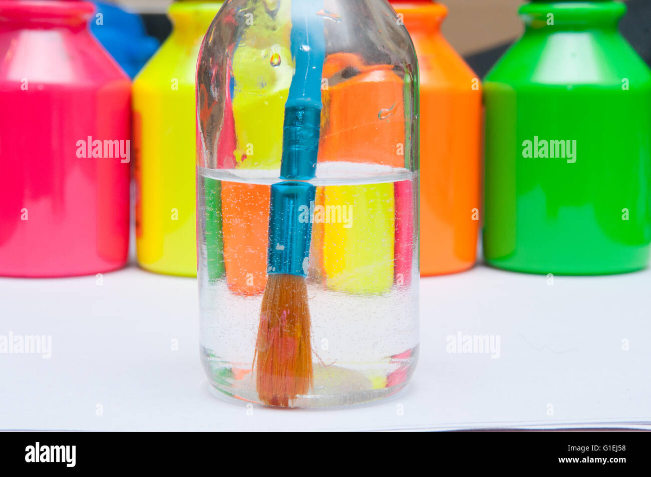 Paint brush in water in front of brightly coloured children's paint