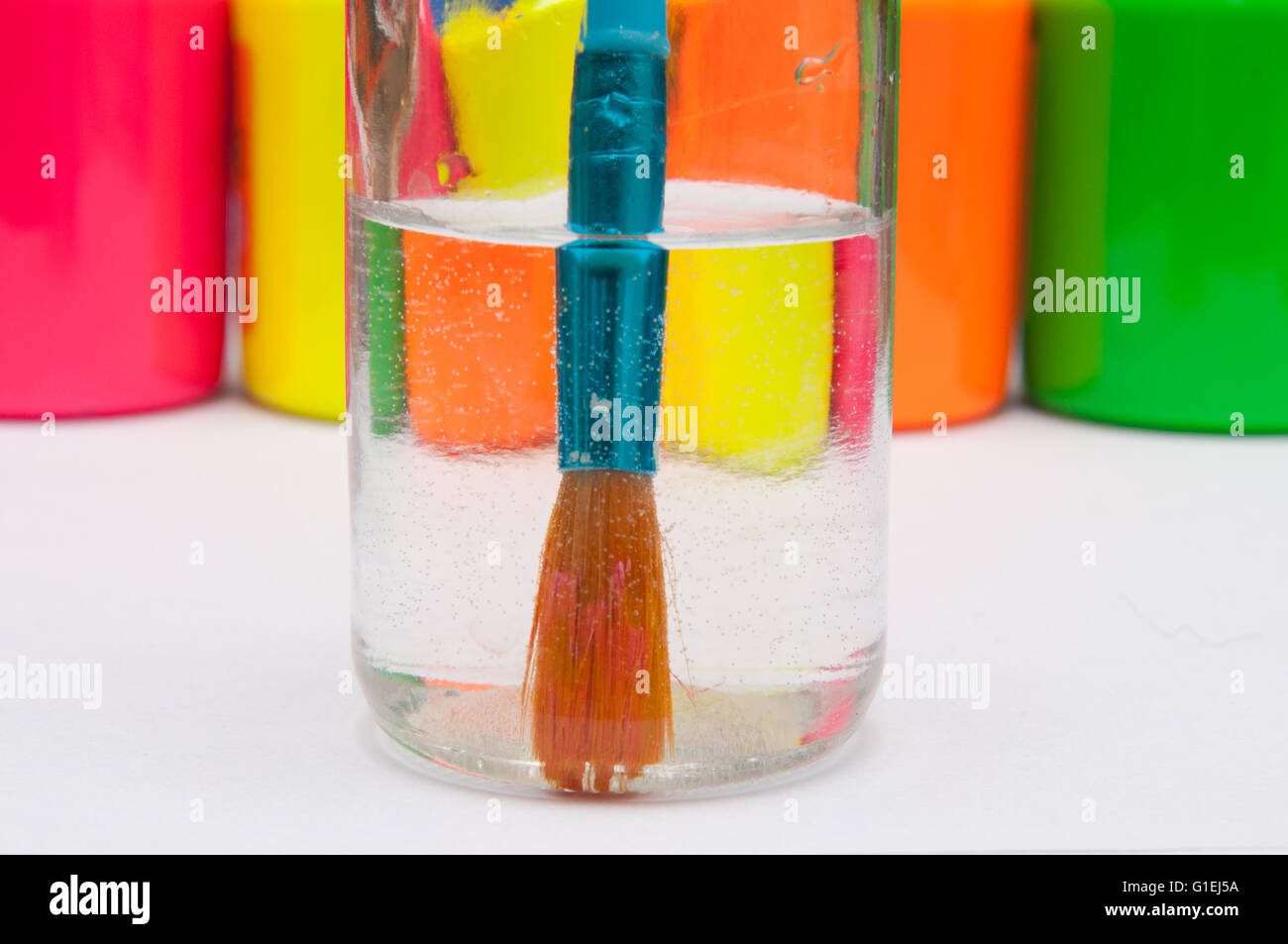 Paint brush in water in front of brightly coloured children's paint