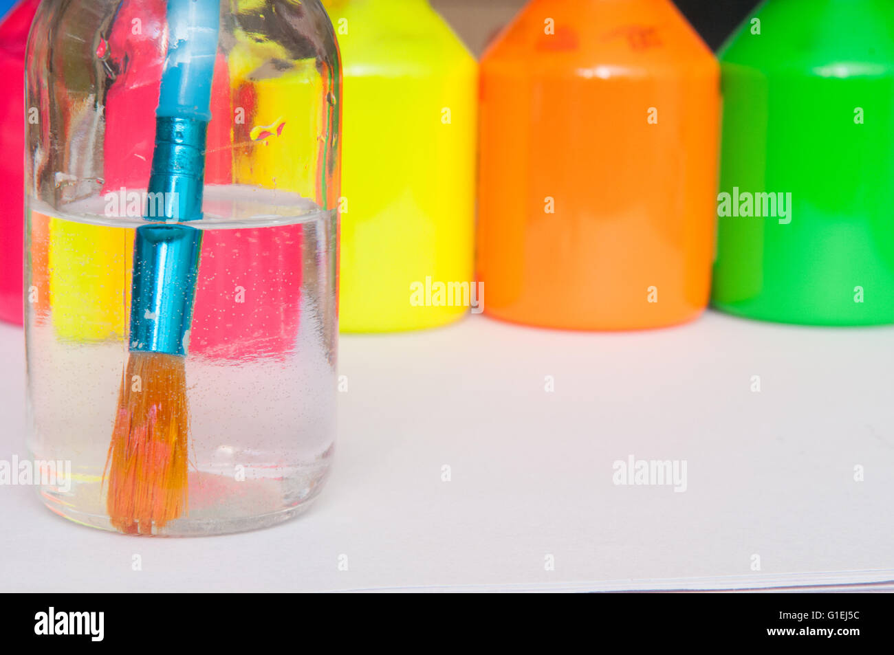 Paint brush in water in front of brightly coloured children's paint