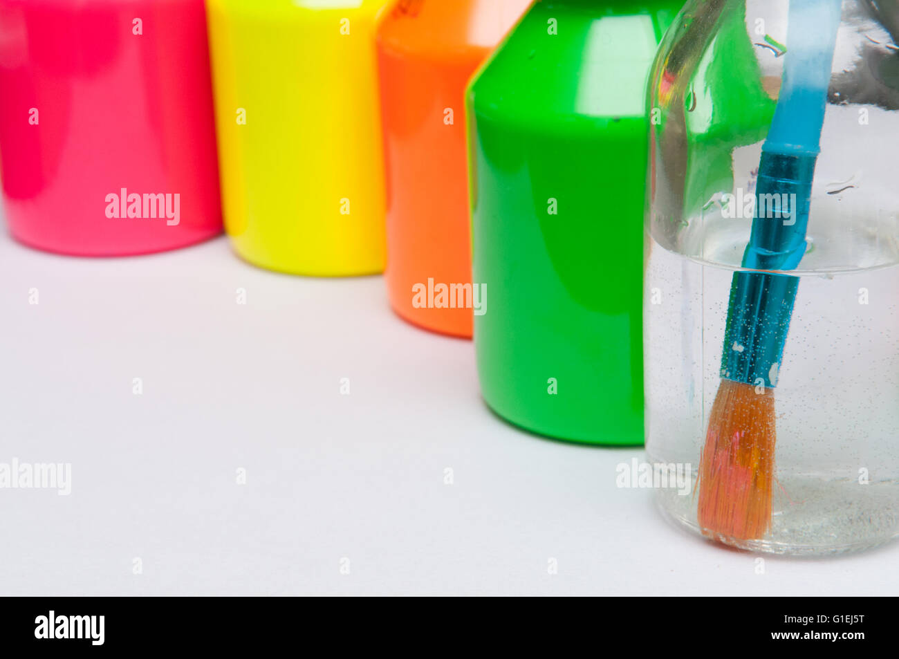 Paint brush in water in front of brightly coloured children's paint