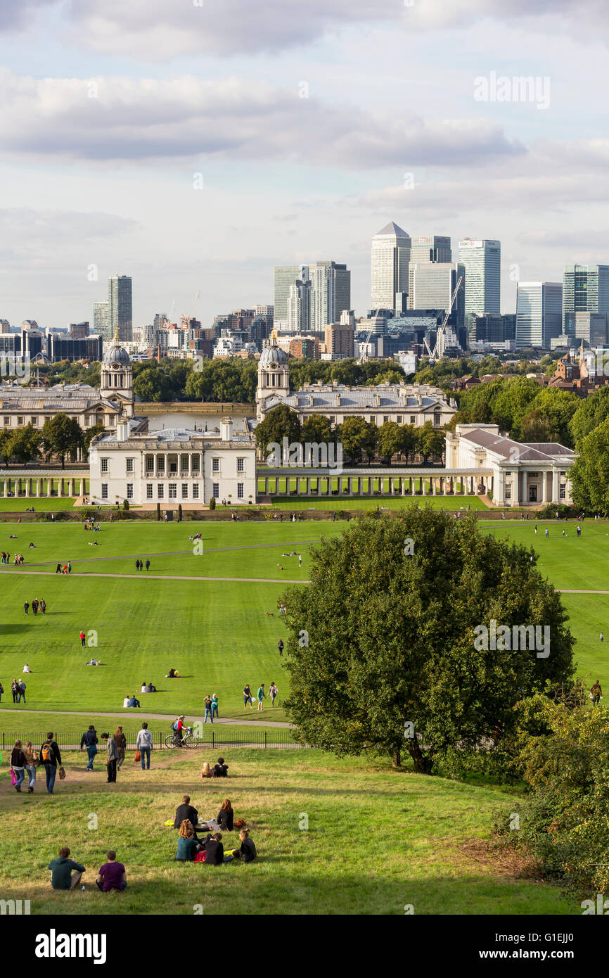 People enjoying a sunny day in Greenwich Park with the landmark buildings of Canary Wharf in the background Stock Photo