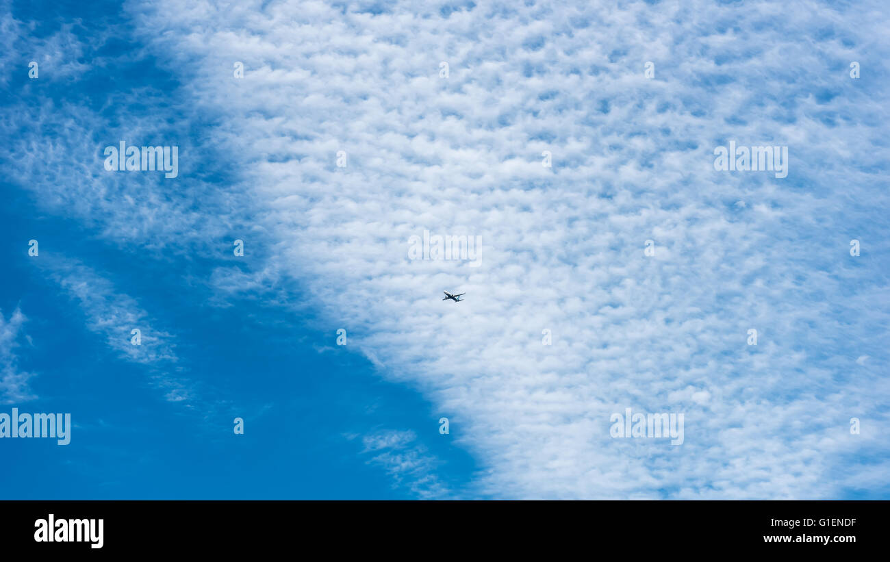 Airplane flying at a height against a brilliant blue sky filled with clouds Stock Photo