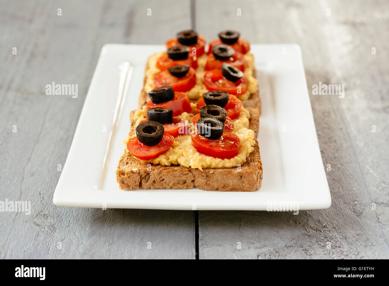 Hummus toasts with cherry tomatoes and black olives. Stock Photo