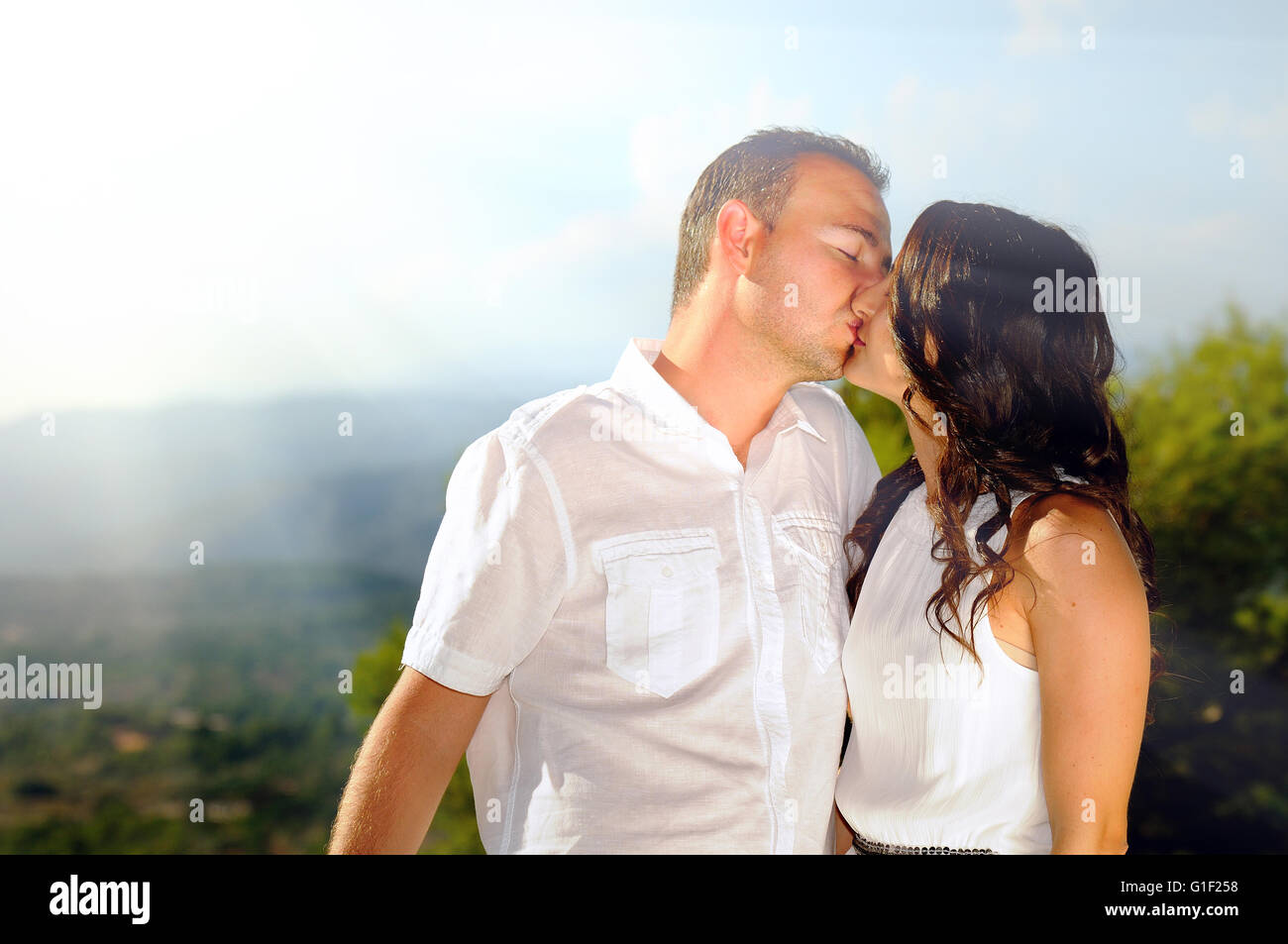 Young couple dressed in white affectionately kissing in the mountains a sunny day Stock Photo