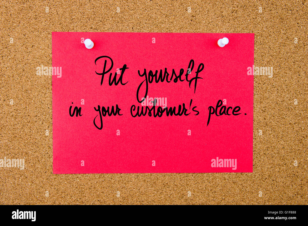 Red paper note with handwritten text Put Yourself In Your Customer place pinned on cork board with white thumbtacks Stock Photo