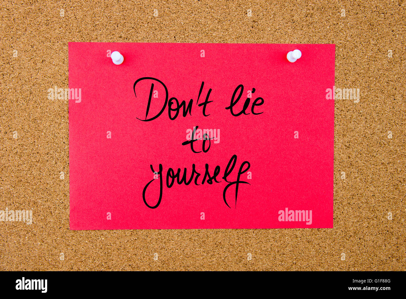 Red paper note with handwritten text Do Not Lie To Yourself pinned on cork board with white thumbtacks Stock Photo