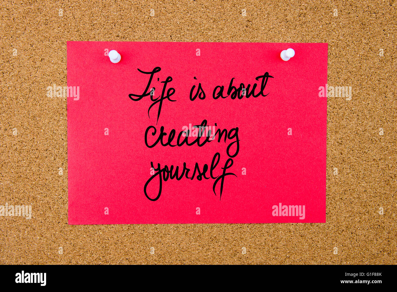 Red paper note with handwritten text Life Is About Creating Yourself pinned on cork board with white thumbtacks Stock Photo