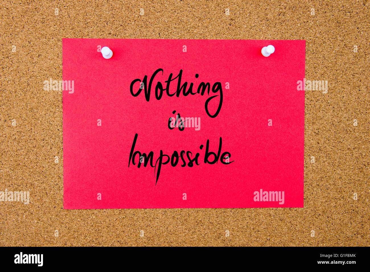 Red paper note with handwritten text Nothing Is Impossible pinned on cork board with white thumbtacks Stock Photo