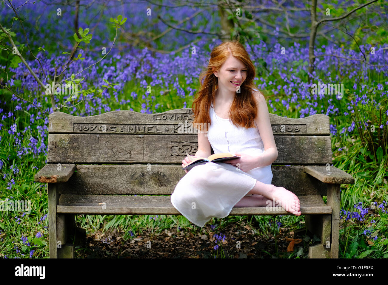 A slender, red-haired young woman in a white dress sits on a wooden ...