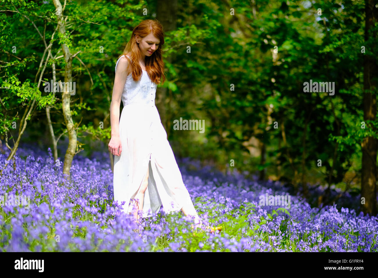 A slender young woman with long red hair and in a long white dress ...