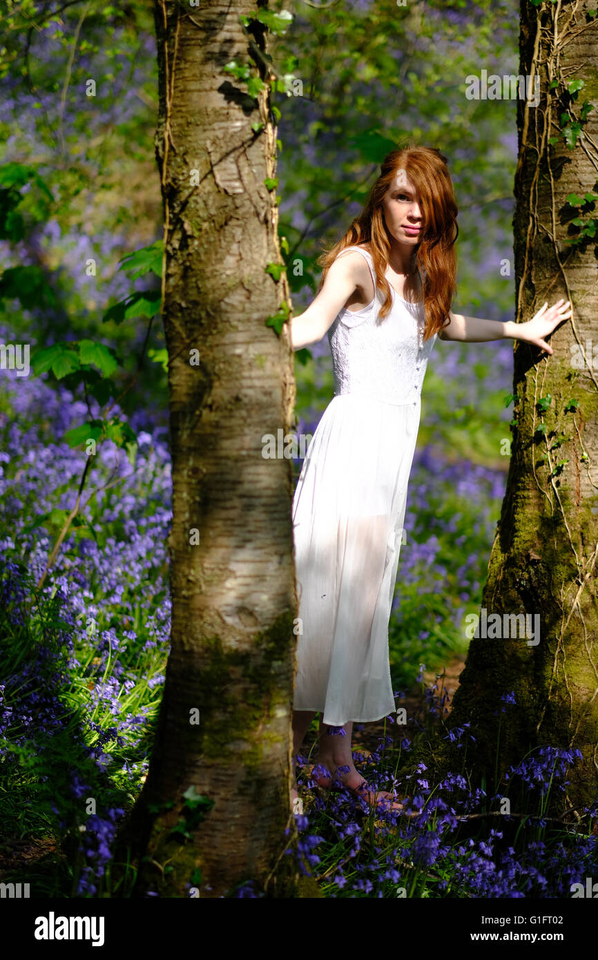 A slender redhaired young woman in a long white dress standing between