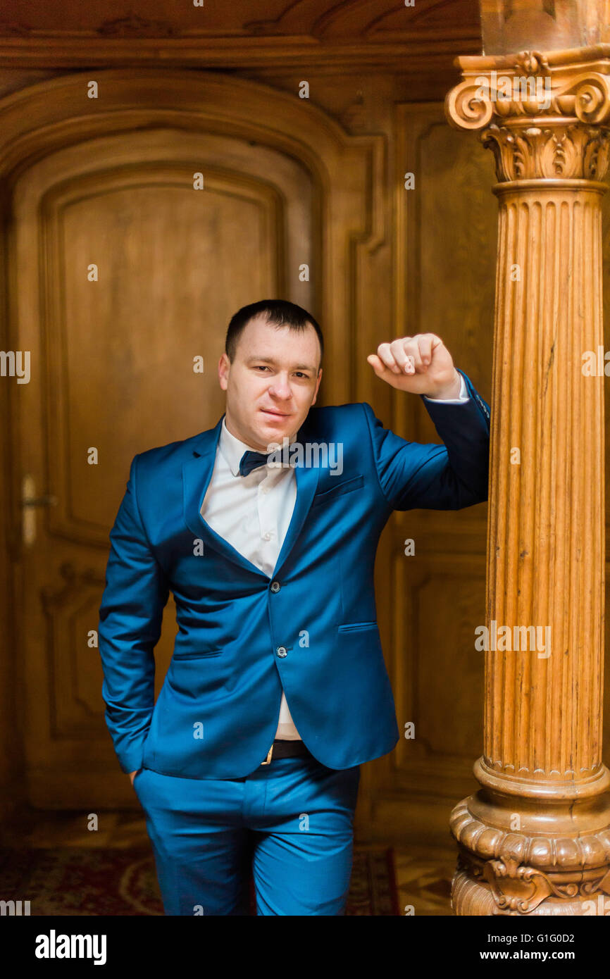 Handsome man in blue suit and bow tie standing at old luxury wooden ...