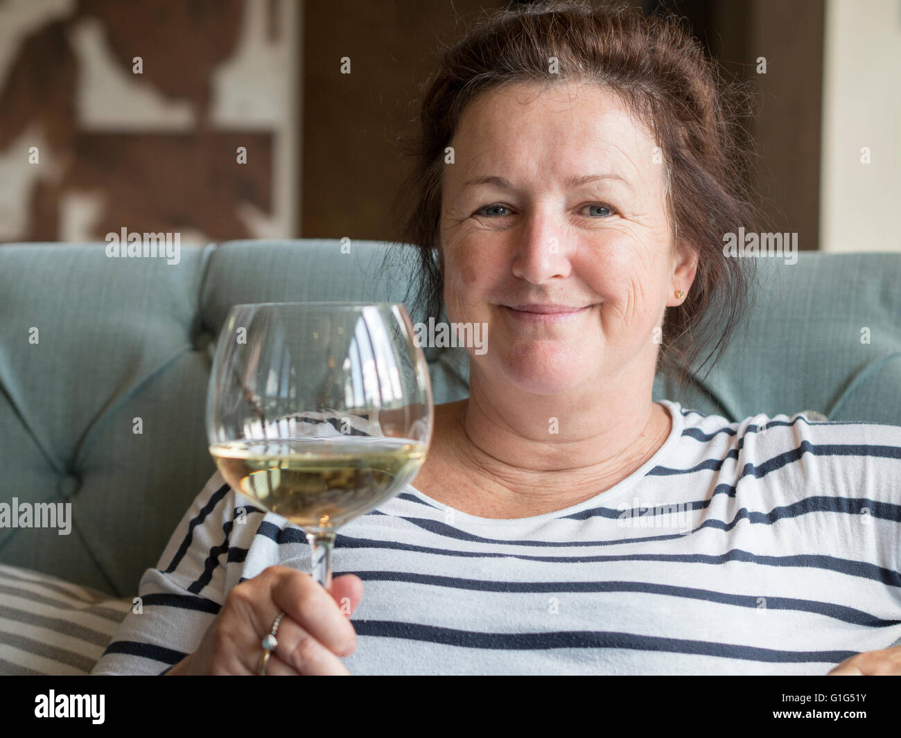 A middle-aged Caucasian woman holding a large glass of white wine. Stock Photo