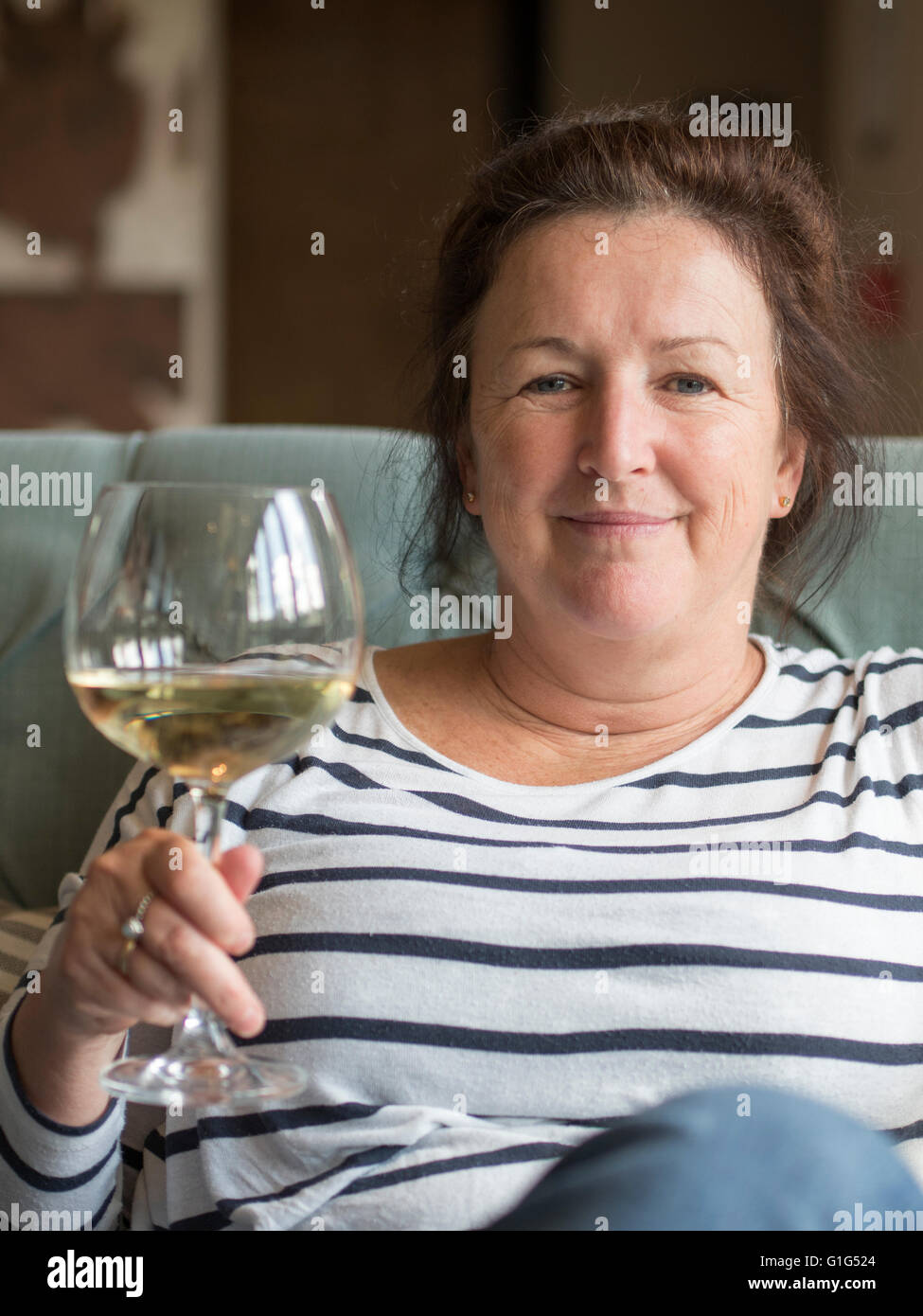 A middle-aged Caucasian woman holding a large glass of white wine. Stock Photo