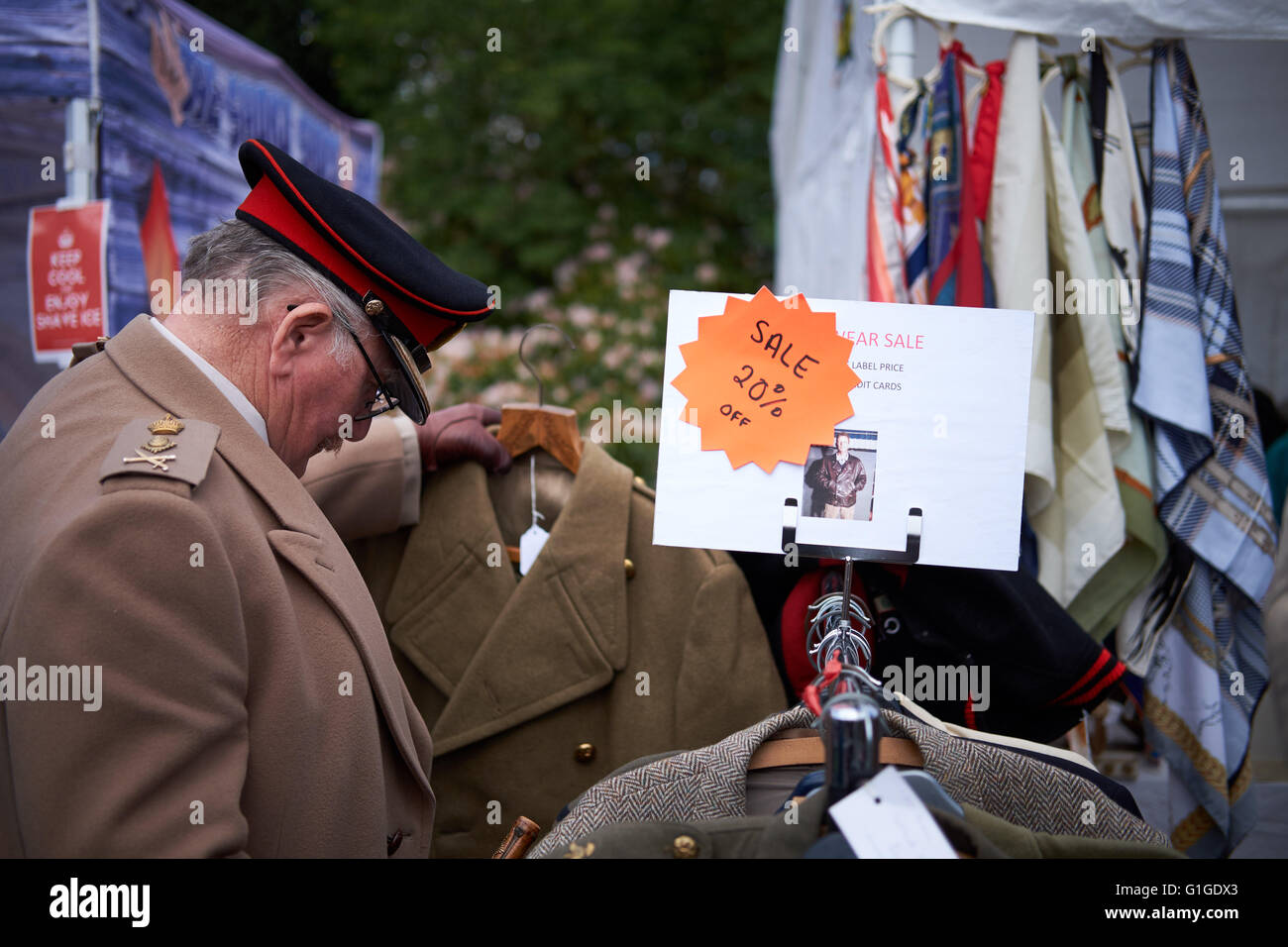 A man dressed in military uniform looks through a sale rack in an outdoor vintage store. Stock Photo