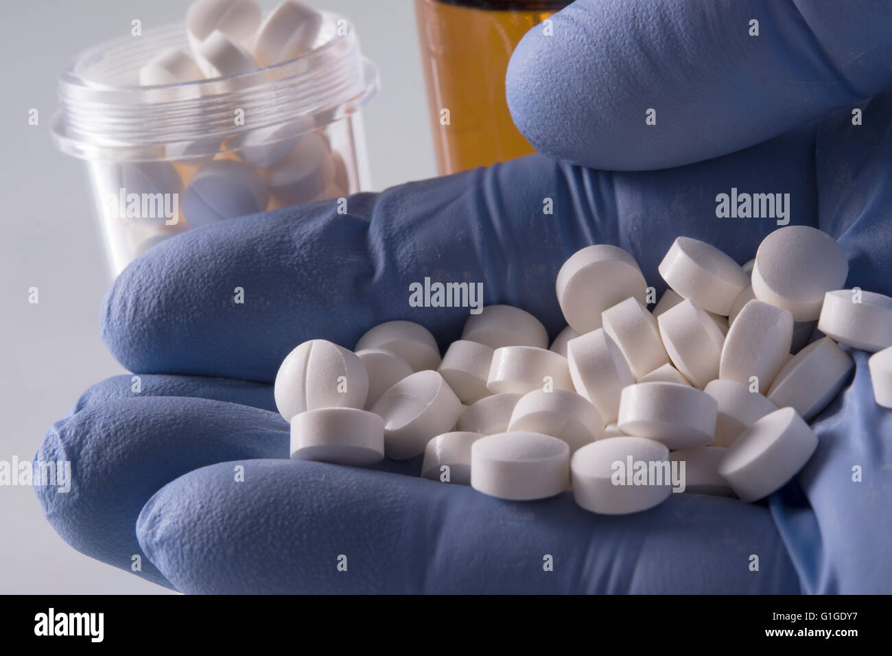 blue gloved hand holding white pills with medication bottles in background Stock Photo