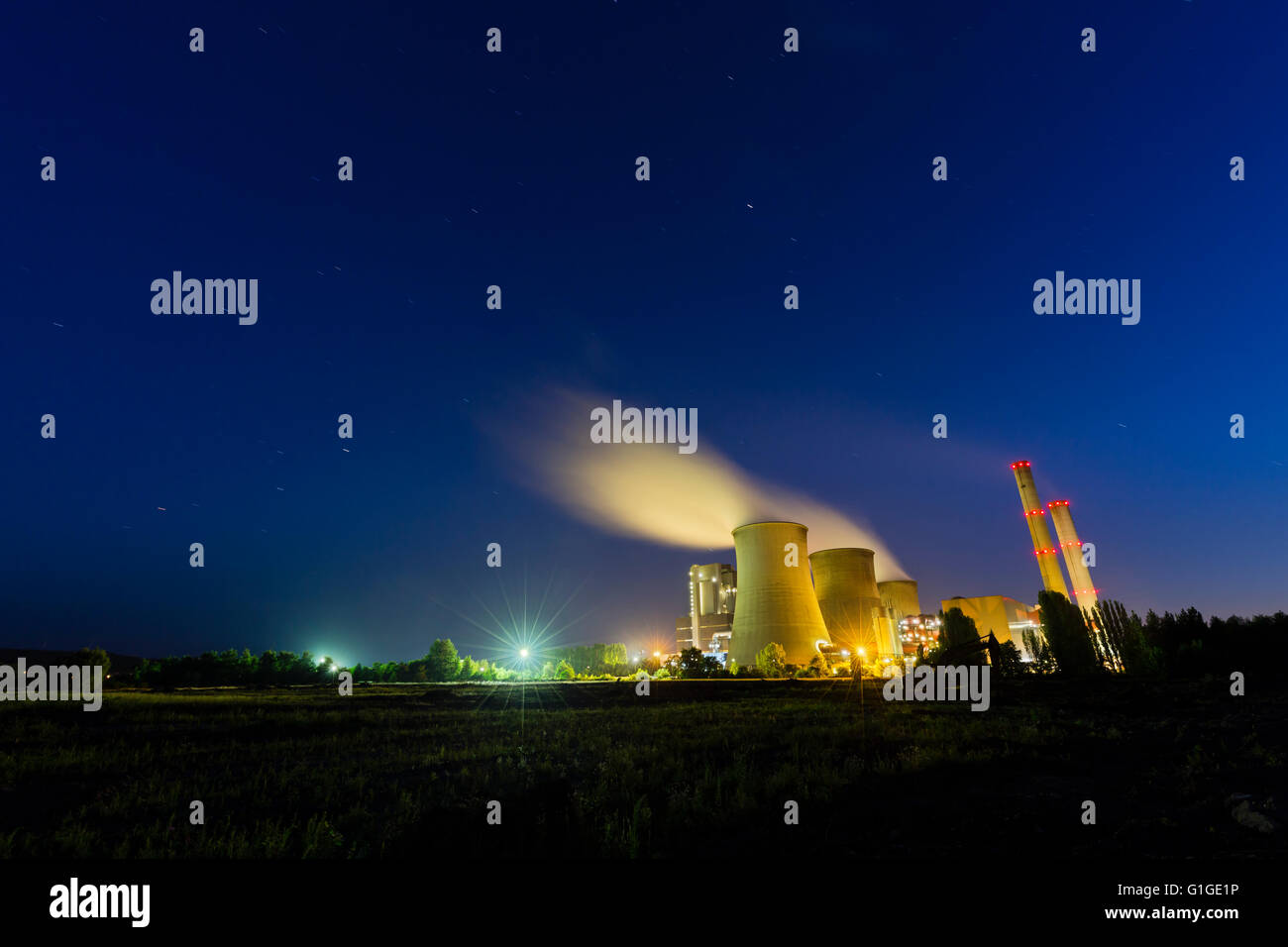 A large coal-fired power plant at night with a lot of steam and deep blue sky with some star trails. Stock Photo