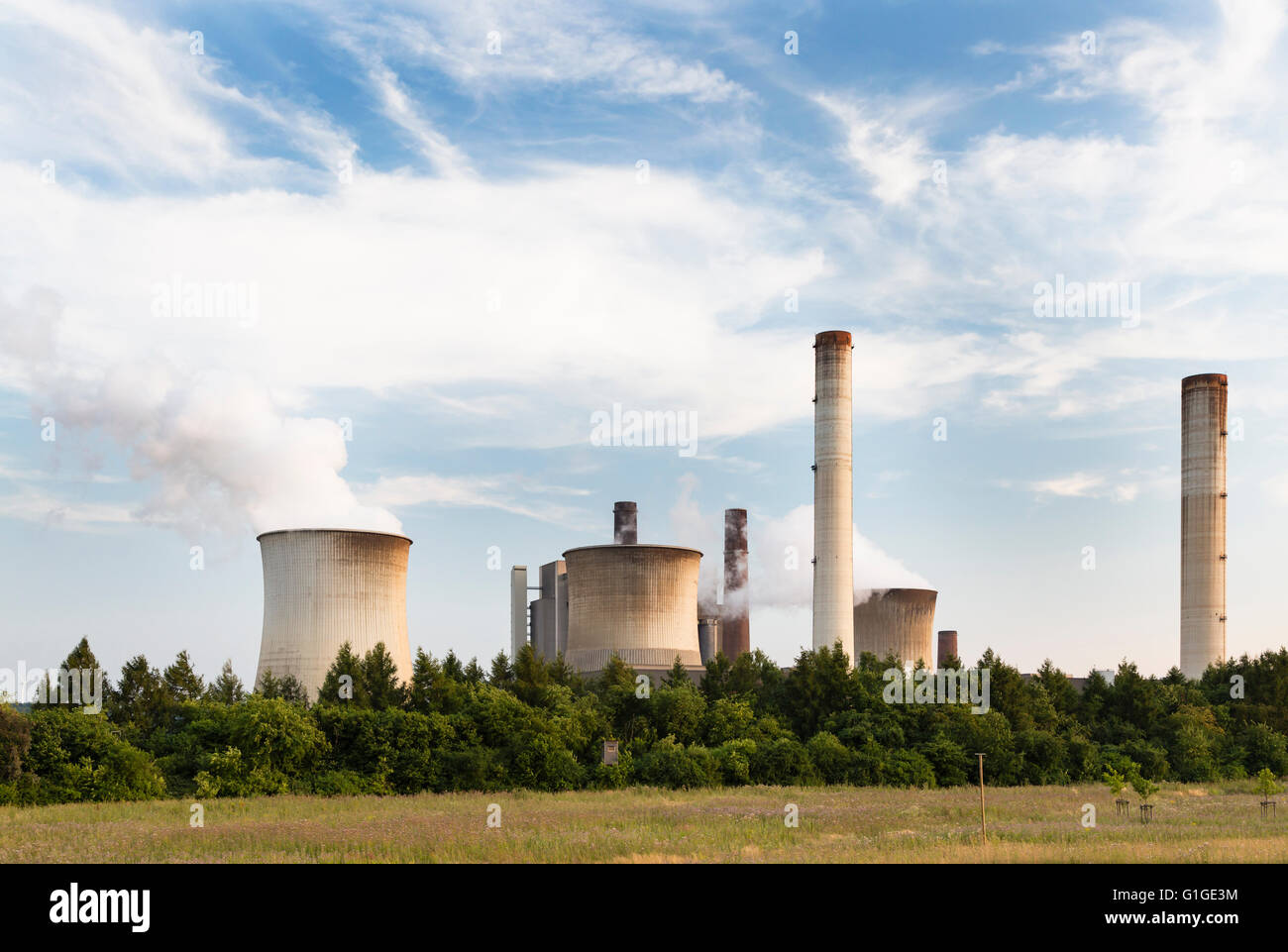 A large coal-fired power station behind some trees and a field. Stock Photo