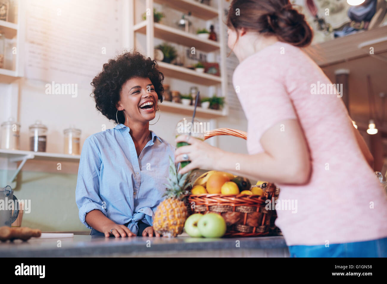 Portrait of young african woman standing behind juice bar counter and talking with female customer holding a glass of fresh juic Stock Photo