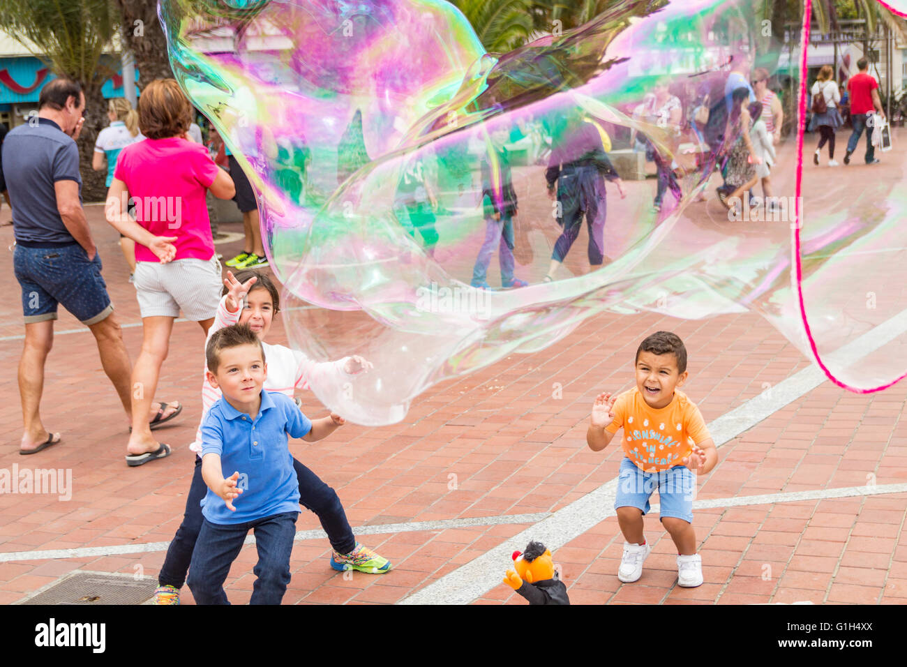 Exited children stand in front of Busker as he makes huge bubbles. Stock Photo