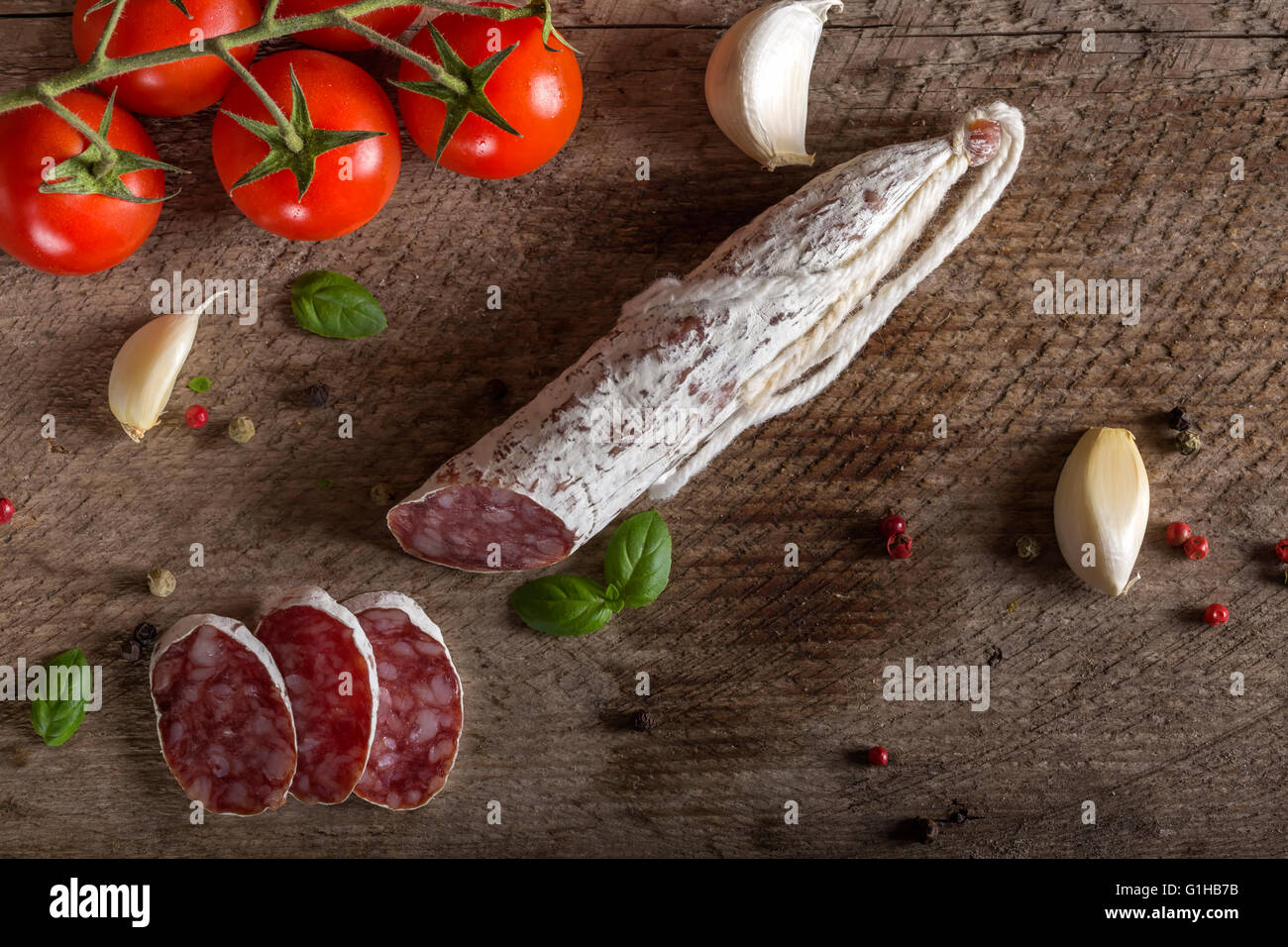 Italian salami with spices and vegetables over rustic wooden background ...