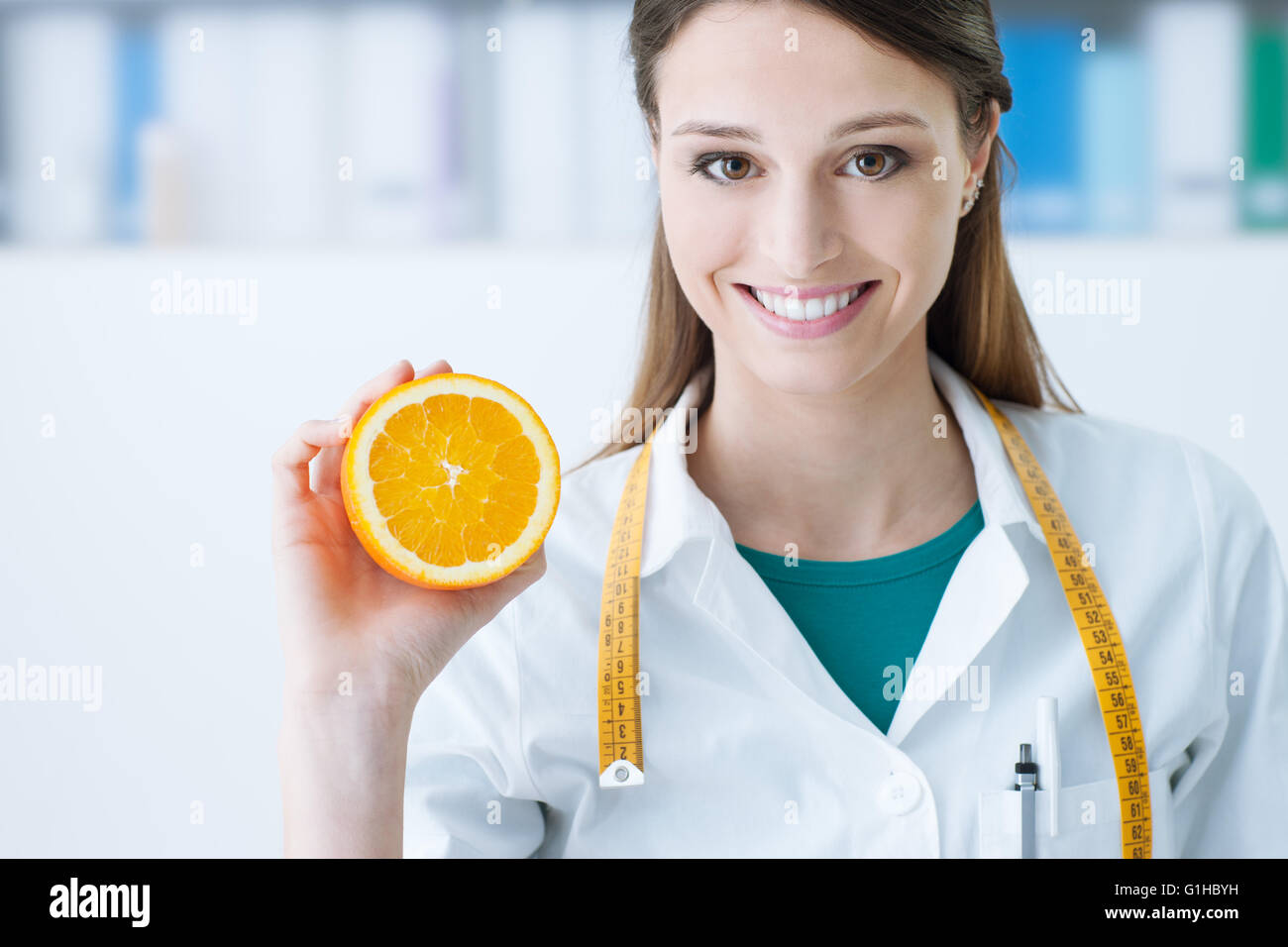 Smiling nutritionist holding a sliced orange, vitamins and healthy diet concept Stock Photo