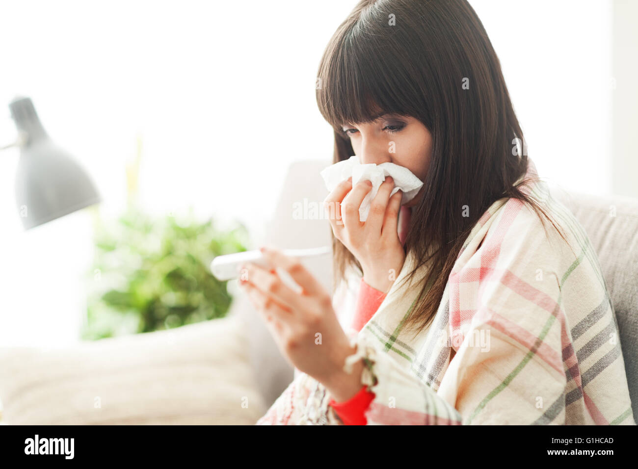Young sick woman with cold and flu, she is blowing her nose and measuring her body temperature Stock Photo